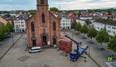 Vor der Friedenskirche auf dem Kehler Marktplatz werden zwei Schiffscontainer für die Freiluftausstellung „Kehler Berge“ aufgestellt.
